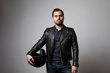Fototapeta premium Portrait of a brutal bearded biker man holding helmet dressed in a black leather jacket. Free space for text.