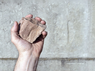 stone in a man’s hand, against the background of a gray concrete wall, selective focus