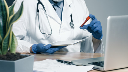 Fototapeta na wymiar Doctor holding blood sample tube and tablet computer for testing in protective gloves in a laboratory.