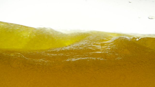 Golden liquid with bubbles on a white background, which was sharply stirred with a teaspoon. Close-up view of beer liquid in a glass bowl. Close-up view of bio fuel shot in a research laboratory.