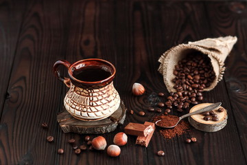 hot fragrant coffee in a vintage clay  cup and coffee beans with nuts on a dark wooden background