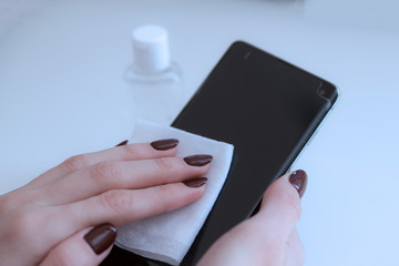 Hand female cleaning her smartphone with microfiber cloth from virus Covid-19. Close up.