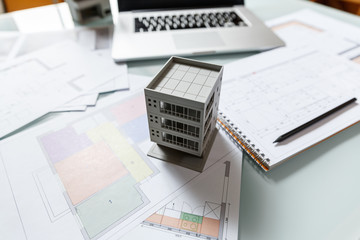 Close up of a house model standing over apartment plans in front of a laptop in a construction bureau.