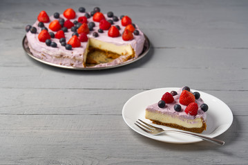 Slice of home made Cheesecake with berries on plate. Cheesecake with Strawberry, blueberry and raspberry on grey wooden background.