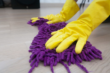 Female hands in a yellow rubber gloves washes a wooden parquet floor. woman in protective gloves wiping up the floor. cleaning floor in house with purple rag