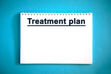 Treatment plan - text on a white notebook on a blue background © Aksana Kavaleuskaya