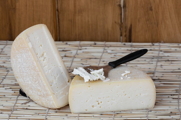 Slice of hard cheese, goat's milk cutting with cheese knife . Typical soft texture and whitish...