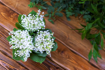 Three bouquets of lilies of the valley on the wet wooden surface with green plants
