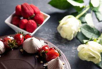 Chocolate cake with fresh strawberry and marshmallows. Fresh  strawberry on the white bowl and white roses on the background.