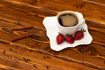 black coffee in whute cup with strawberry, cinnamon and spices