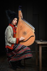 Gorgeous young woman in ukrainian traditional costume with ukrainian musical instrument bandura  Portrait of attractive woman in hat with red lips.