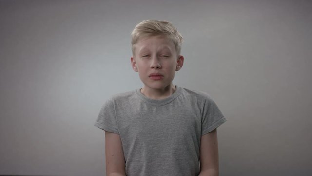Blonde caucasian kid is showing the importance of sneezing into an elbow in order to prevent the spread of Covid19 infection
