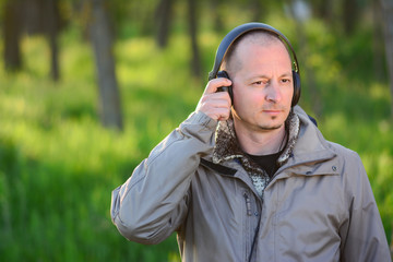 man resting in park and listening to music. middle aged man standing on grass with cellphone and black wired headphones. Leisure and connection concept