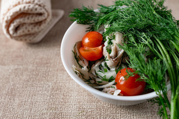 Marinated oyster mushrooms, garnished with cherry tomatoes and green dill. A dish with onions and butter in a white plate with a beige light cloth on the table