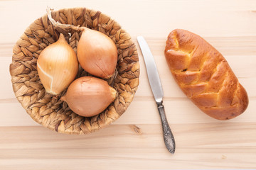 Fresh bread, onions and a vintage knife on a light wooden background. Viewed from above