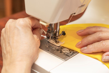 Woman hands using the sewing machine to sew the face medical mask. Homemade protective mask against virus.