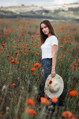 Young cute girl with hat at red poppies field. - 345997234
