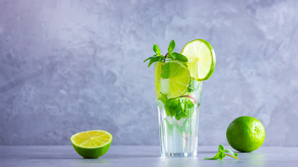 Mojito cocktail with lime and mint in tall glass. Fresh mojito in glass on a gray background. Refreshing mint cocktail with lime. Infused water. Copy space