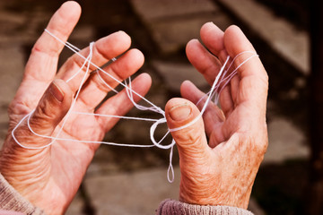 Old wrinkled hands are tangled in a white thread. An old grandmother is trying to untangle her...