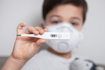a masked child holds a thermometer with a high temperature