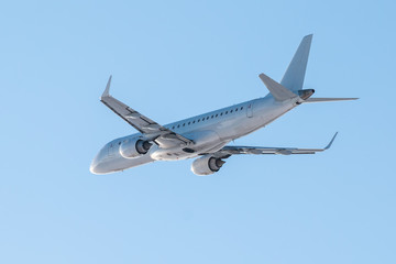 Modern white passenger aircraft flies in the air on a clear sunny day against a clear blue sky