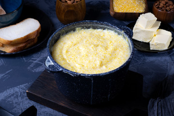 Corn porridge with milk in a black saucepan against the dark background