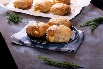 Puff buns with cheese on the ceramic plate and on the baking parchment with herbs around