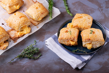 Puff buns with cheese on the ceramic plate and on the baking parchment with herbs around