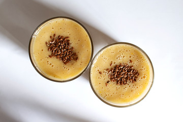 Two glasses with orange-banana smoothie on a white table