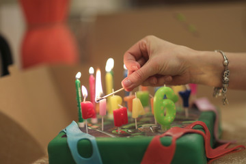 Woman lights wax candles with a burning match on a festive cake with congratulations
