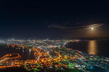 Hakodate City night view from Mt. Hakodate observatory, big bright moon light up the sea, golden reflection on surface. Famous scenic spot in the world. Hokkaido, Japan