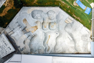 Aerial view of big concrete skate park with lots of pools, ramps and obstacles surrounded by green grass - a place for skateboarders, skaters, bikers. 