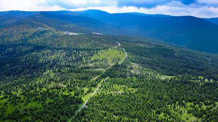 Aerial view of Krkonoše Mountains in the Czech Republic during summertime, green coniferous trees, and trekking trail seen from above.