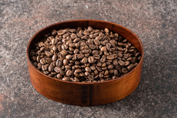 Roasted coffee beans in a wooden box on a dark background.