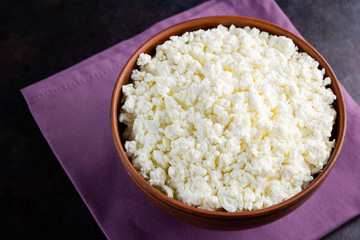 Cottage cheese on a dark background. Fresh cottage cheese in a bowl. Clay plate with soft cheese on a linen napkin. Minimalism. Top view. Copy space