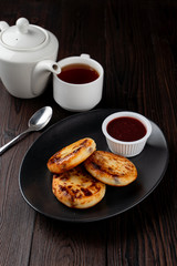 Fried russian cottage cheese patties on black plate on dark wooden table