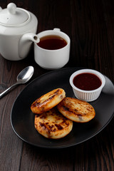 Fried russian cottage cheese patties on black plate on dark wooden table
