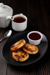 Fried russian cottage cheese patties on black plate on dark wooden table