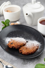 American crunchy chocolate cookies with powdered sugar on top, served with tea in white single tea-set