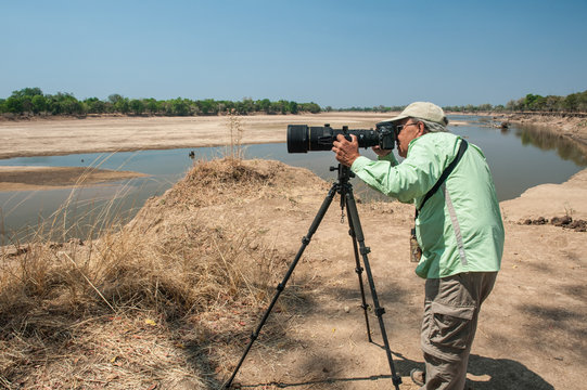 A photographer shooting in a National Park in Africa with a big telephoto lens and tripod