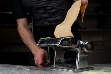 Chief is rolling raw dough in a spaghetti machine to make homemade spaghetti, only male hands visible, close up shot