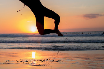 Piernas de un chico con neopreno saltando en la arena de la playa durante la puesta de sol.