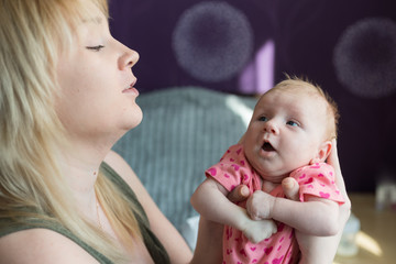 A woman holds a small newborn girl in her arms. The daughter looks at her mother. Mothers love and care