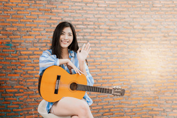 Beautiful Asian female musician performing live in front of audience recording viral video on social media singing playing guitar taking to people, camera vlogging at working at home brick background