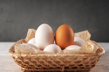 One orange egg among white in one wicker basket.