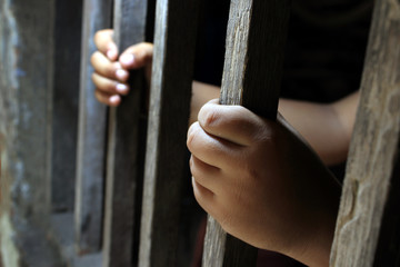 Hands of a young child clutching prison bars. Child in jail. Sad little boy forced to stay at home as the pandemic coronavirus, covid19. 