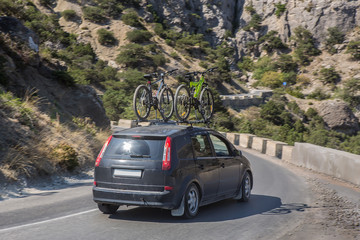 car with bicycles on the upper trunk moves on a road in the mountains