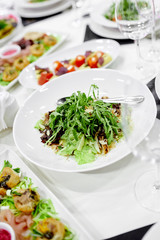 vegetable green salad with ruccola stands on a table with a white tablecloth and in a white plate on the table 