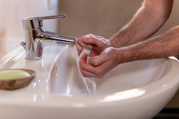 Caucasian man thoroughly cleaning hands and fingernails with a brush in wash basin under running...