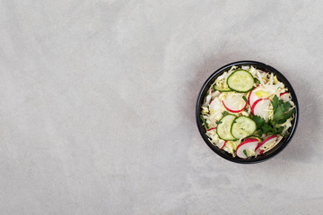 Vegan salad with fresh cabbage, radish, cucumber and parsley on a light gray background top view